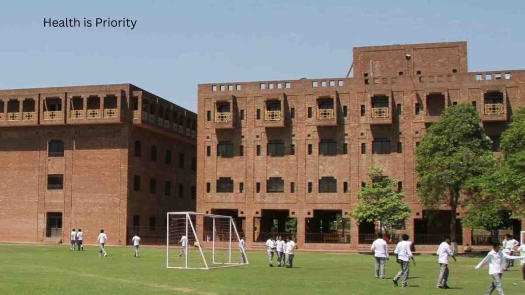 Students standing on a school playground in front of a large brick school building in Punjab.
