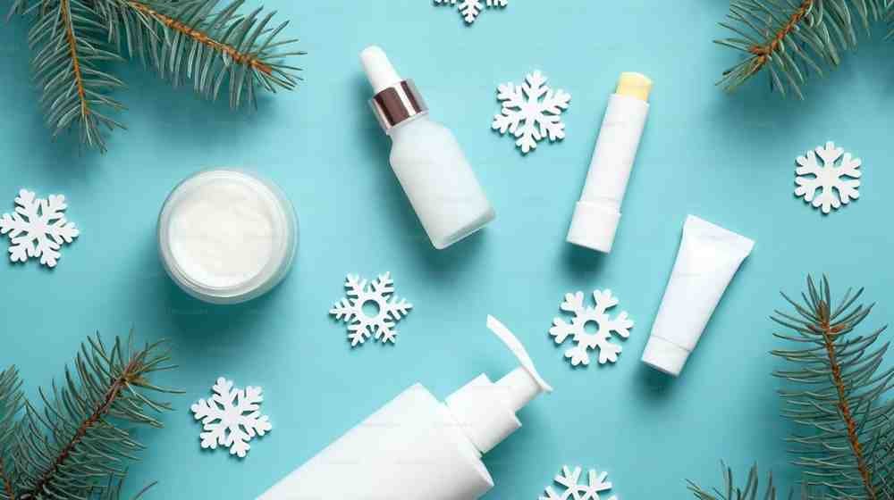 Winter skincare products arranged on a blue background with snowflakes.