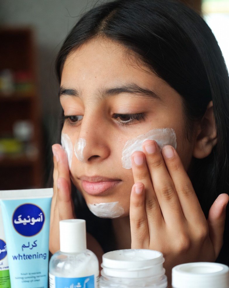 Close-up of a person applying skin whitening cream on the face with visible skincare products nearby