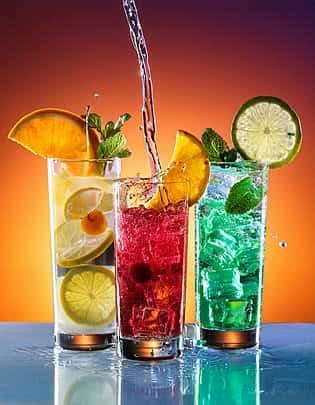 Glasses of refreshing summer drinks with ice and fruit served on a table on a hot day