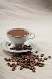 A steaming cup of coffee placed on a wooden table with coffee beans around it