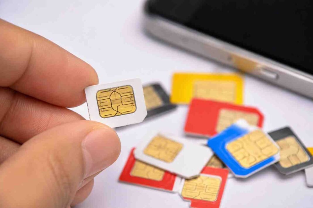 simsale Hand holding a SIM card with multiple mobile SIMs and smartphone in the background