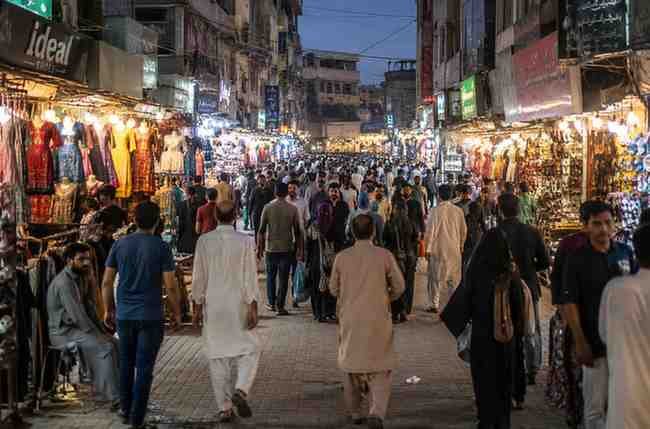 Busy shopping bazaar in Pakistan during evening hours with shoppers and illuminated retail stores.