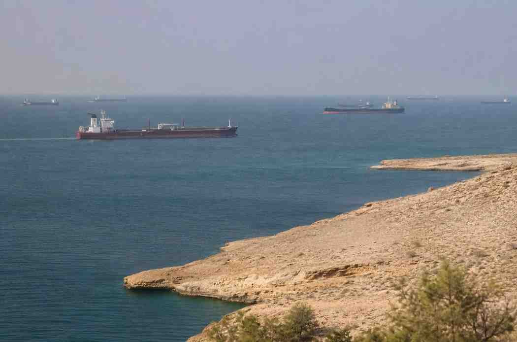 Cargo ships sailing through the Strait of Hormuz under clear skies near the Iranian coastline.