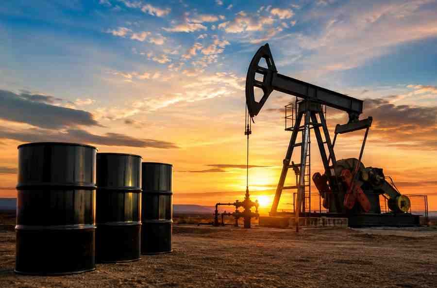 Oil pumpjack and crude oil barrels at a production site during sunset.