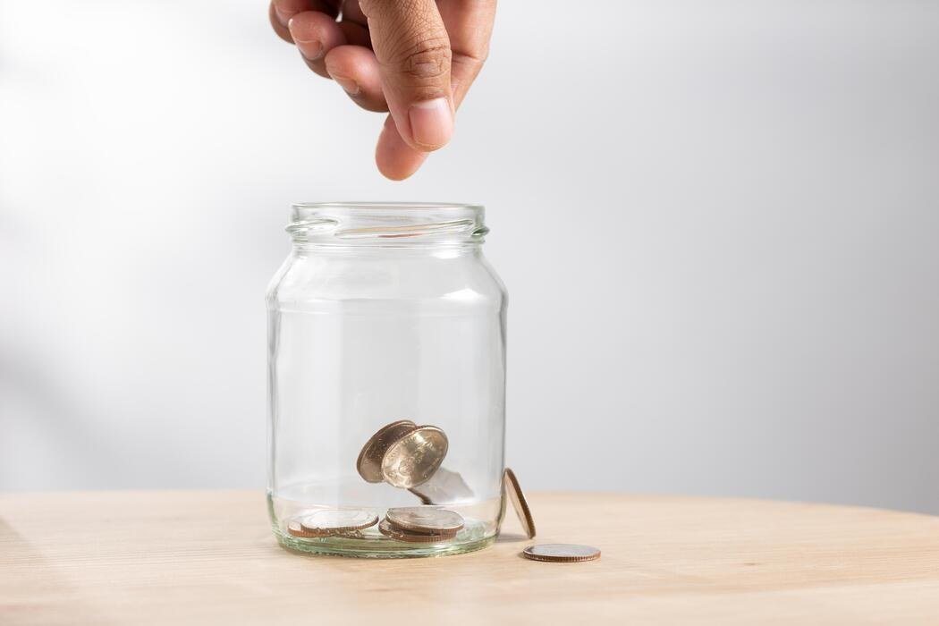 The 52-Week Savings Challenge: A Complete 2026 Playbook Hand dropping a coin into a glass savings jar